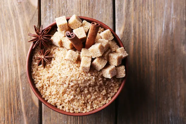 Brown sugar cubes and crystal sugar in bowl on wooden background