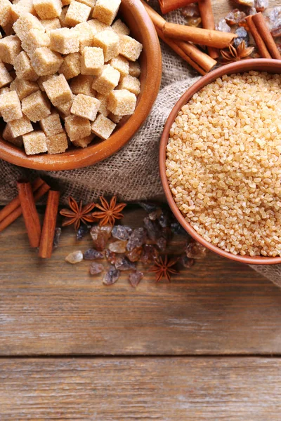 Brown sugar cubes, reed and crystal sugar in bowl with spices on wooden background — Stock Photo, Image