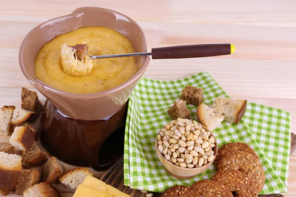 Fondue, biscuits, slices of cheese and rusks on cutting board on napkin on wooden background — Stock Photo, Image