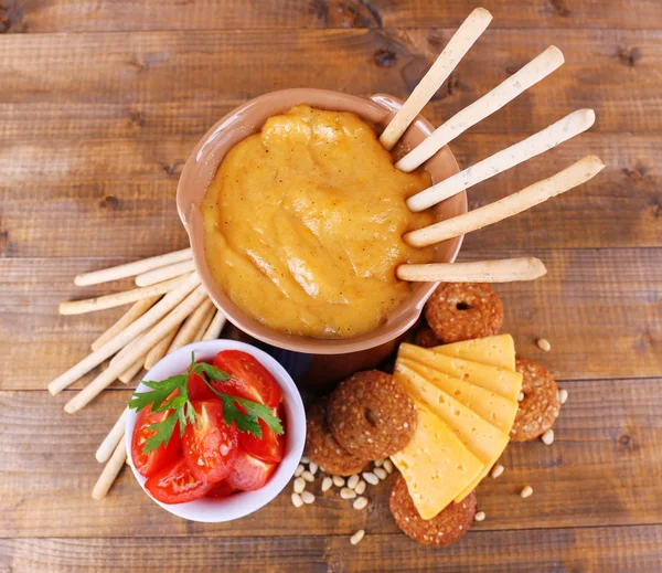 Fondue, fatias de queijo, tomates e biscoitos sobre fundo de madeira — Fotografia de Stock