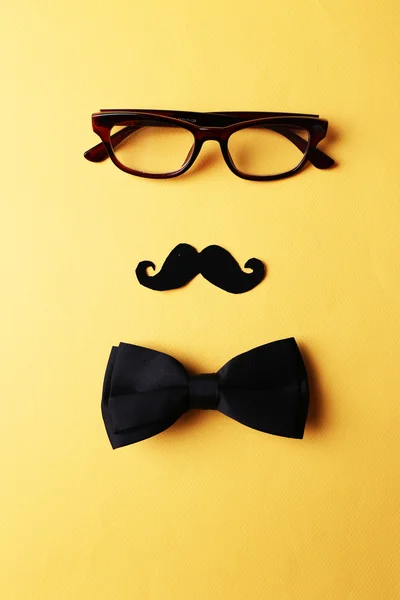 Glasses, mustache and bow tie forming man face on yellow background — Stock Photo, Image