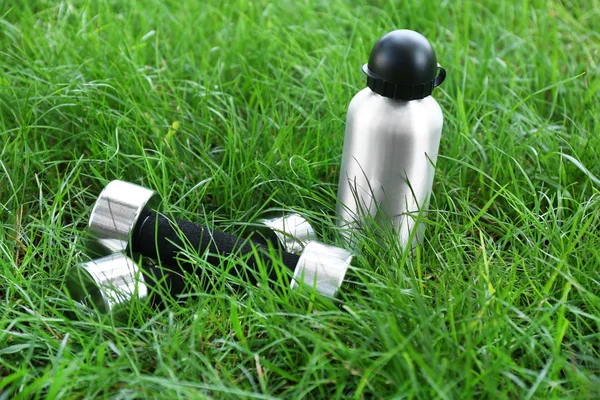 Halteres e garrafa com água no fundo grama verde — Fotografia de Stock