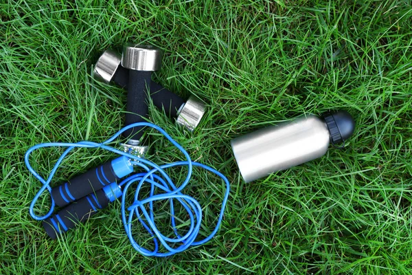 Dumbbells and bottle with water on green grass background — Stock Photo, Image