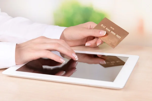 Руки женщины держат кредитную карту и планшет на столе на ярком фоне — стоковое фото
