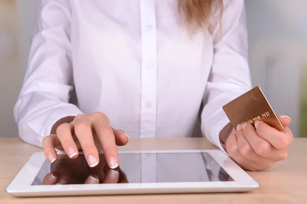 Manos femeninas sosteniendo la tarjeta de crédito y la tableta del ordenador en la mesa sobre fondo brillante — Foto de Stock