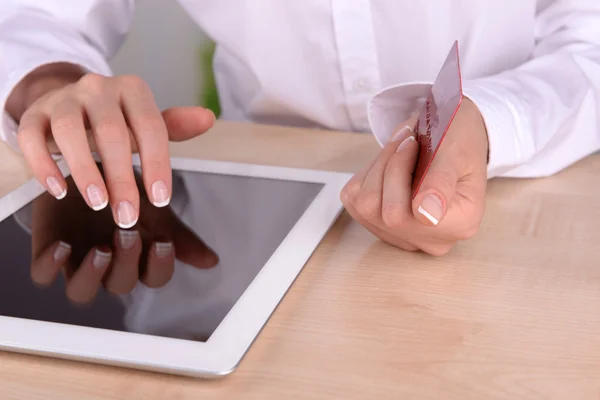 Manos femeninas sosteniendo la tarjeta de crédito y la tableta del ordenador en la mesa en primer plano — Foto de Stock