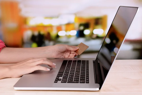 Mãos femininas segurando cartão de crédito e laptop na mesa em fundo brilhante — Fotografia de Stock