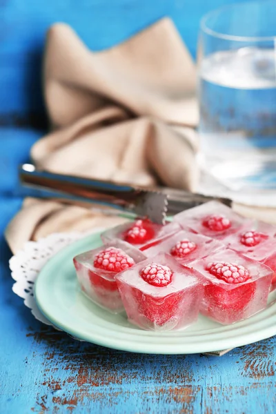 Ice cubes with raspberry on plate, on color wooden background — Stock Photo, Image