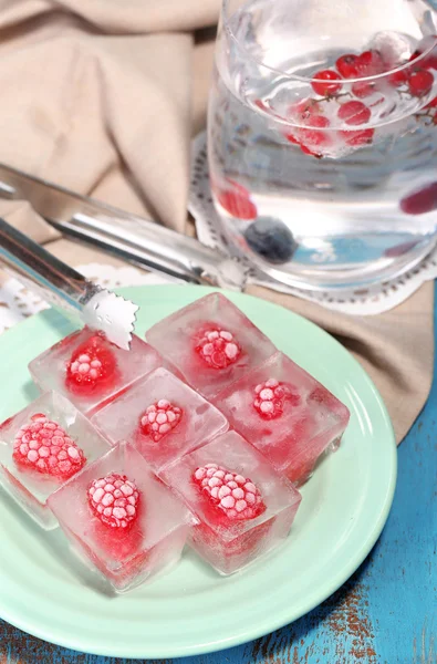 Cubos de hielo con frambuesa en placa, sobre fondo de madera de color — Foto de Stock