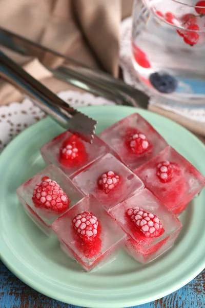 Ice cubes with raspberry on plate, on color wooden background — Stock Photo, Image