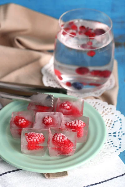 Ice cubes with raspberry on plate, on color wooden background — Stock Photo, Image