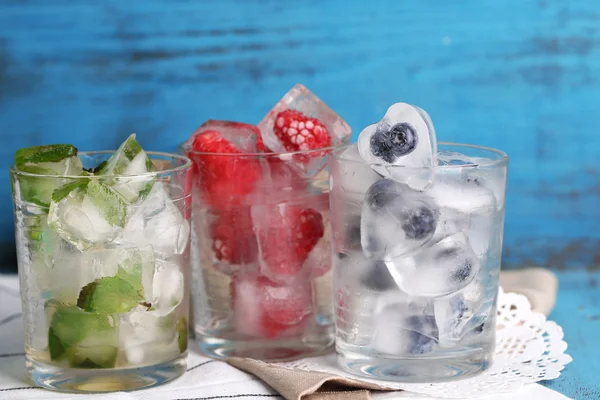 Cubos de hielo con hojas de menta, frambuesa y arándano en vasos, sobre fondo de madera de color —  Fotos de Stock