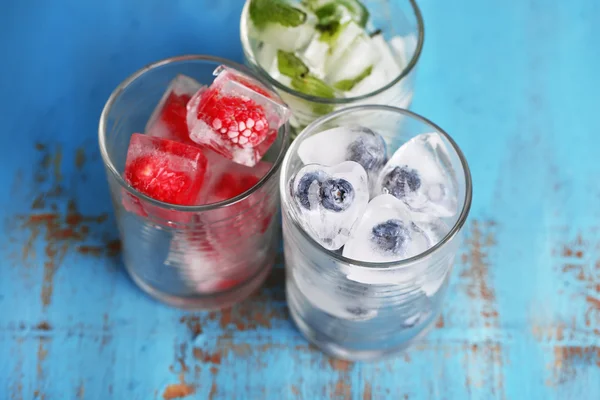 Cubos de hielo con hojas de menta, frambuesa y arándano en vasos, sobre fondo de madera de color —  Fotos de Stock