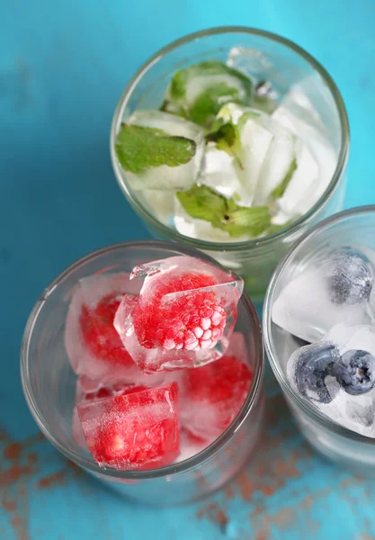 Cubes de glace aux feuilles de menthe, framboises et bleuets dans des verres, sur fond de bois couleur — Photo