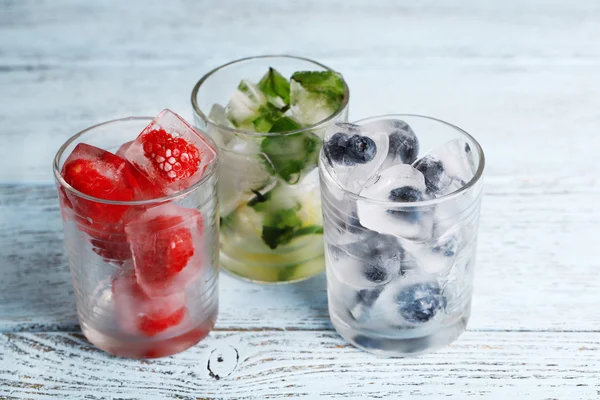 Cubes de glace aux feuilles de menthe, framboises et bleuets dans des verres, sur fond de bois couleur — Photo