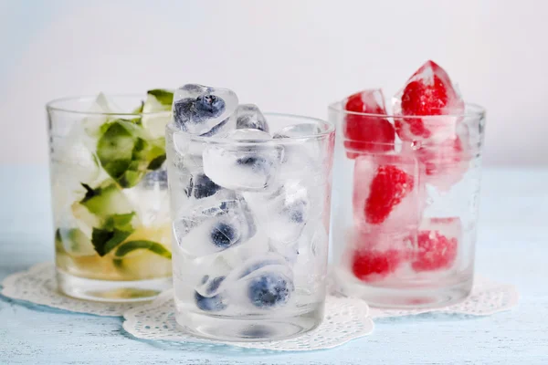 Cubes de glace aux feuilles de menthe, framboises et bleuets dans des verres, sur fond de bois couleur — Photo