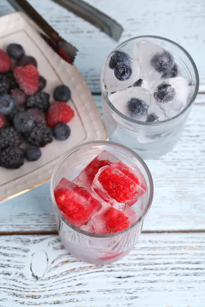 Gefrorene Beeren und Eiswürfel mit Minzblättern, Himbeere und Blaubeere im Glas, auf farbigem Holzgrund — Stockfoto