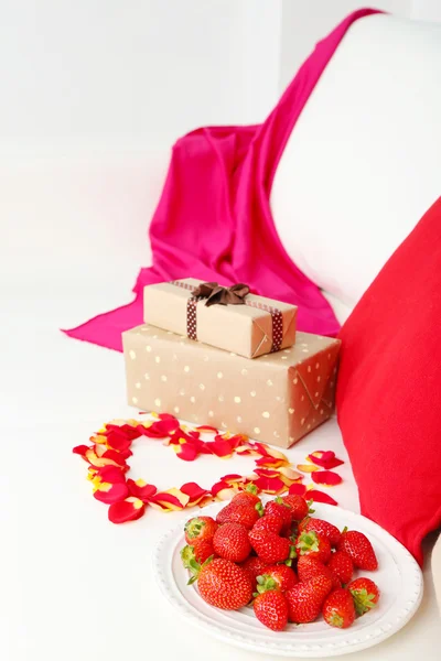 Romantiska Stilleben med jordgubb, gåvor och kronblad av rosor på soffa — Stockfoto