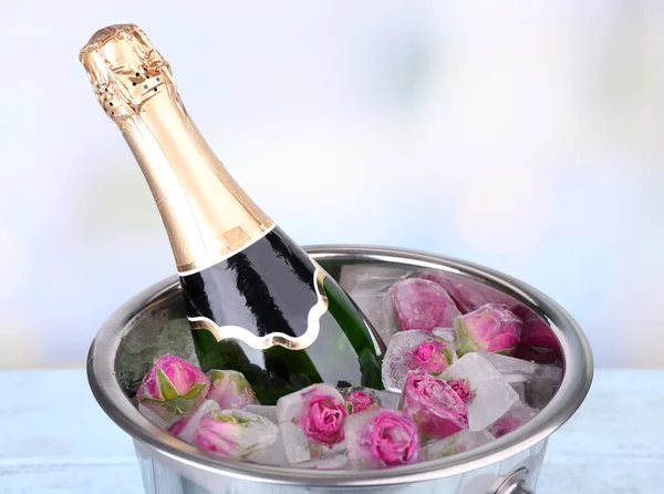 Frozen rose flowers in ice cubes and champagne bottle in bucket, on light background — Stock Photo, Image