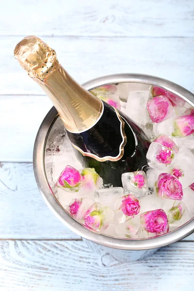 Frozen rose flowers in ice cubes and champagne bottle in bucket, on light background — Stock Photo, Image