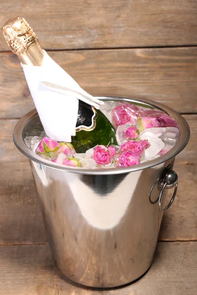 Замороженные цветы роз в кубиках льда и бутылка шампанского в ведре, на деревянном фоне — стоковое фото