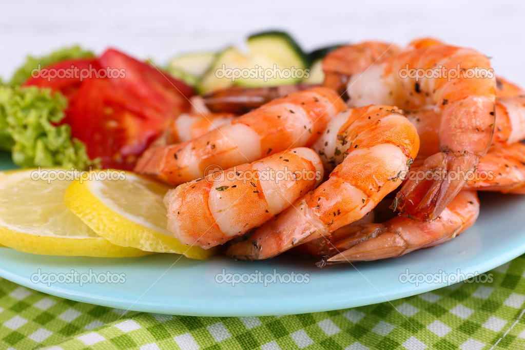 Plate of fresh boiled prawns with tomatoes, lettuce, lemon and avocado on a napkin on wooden background