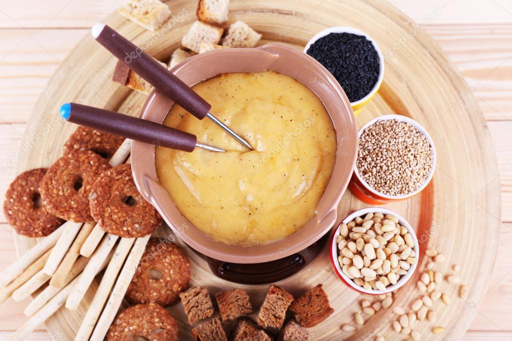 Fondue, biscuits, spices and rusks on bamboo plate on wooden background