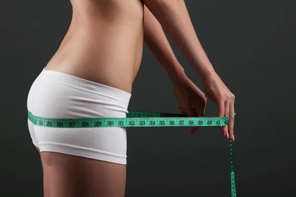 Beautiful young woman measuring her body with tape on gray background — Stock Photo, Image