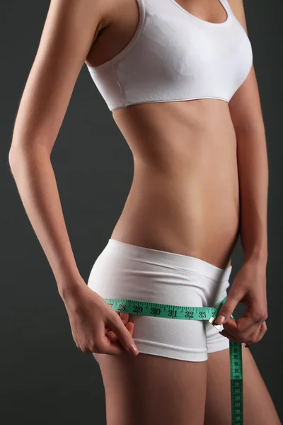 Hermosa mujer joven midiendo su cuerpo con cinta adhesiva sobre fondo gris — Foto de Stock
