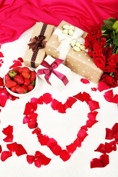 Romantisches Stillleben mit Erdbeeren, Geschenkschachteln und Rosenblättern auf dem Bett — Stockfoto