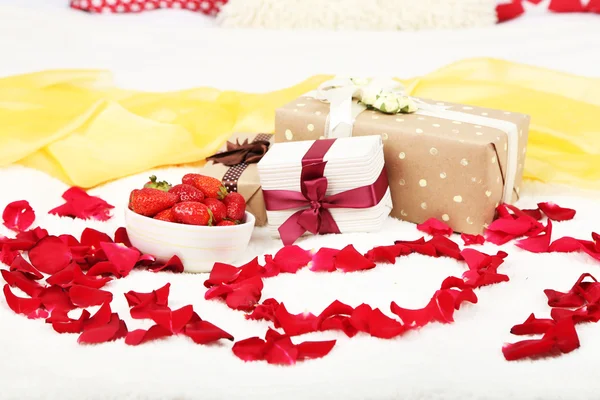 Romântico ainda vida com morango, caixas de presente e pétalas de rosas na cama — Fotografia de Stock