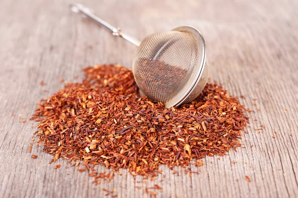 Té rooibos seco en colador de té sobre mesa de madera —  Fotos de Stock