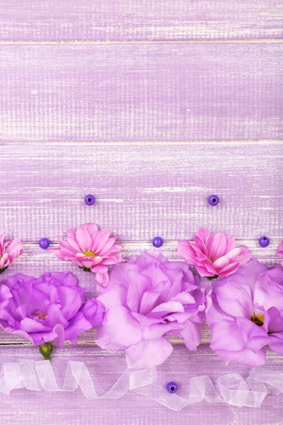 Beautiful chrysanthemum and artificial eustoma flowers on purple wooden background — Stock Photo, Image