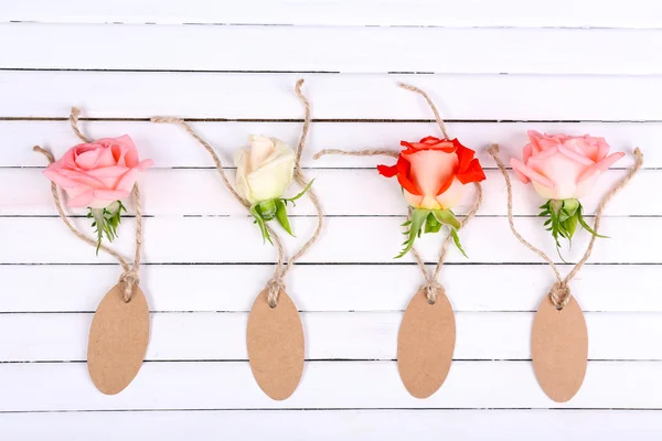 Beautiful roses and empty tags on white wooden background — Stock Photo, Image