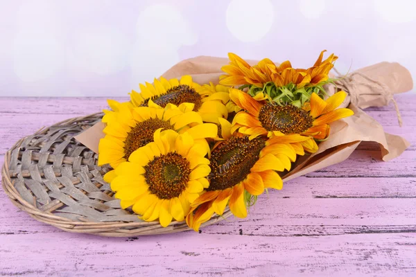 Beautiful sunflowers in pitcher on wicker stand on table on bright background — Stock Photo, Image