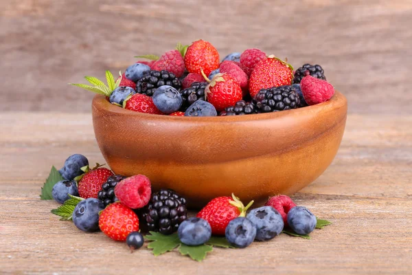 Ripe sweet different berries in bowl, on old wooden table — Stock Photo, Image