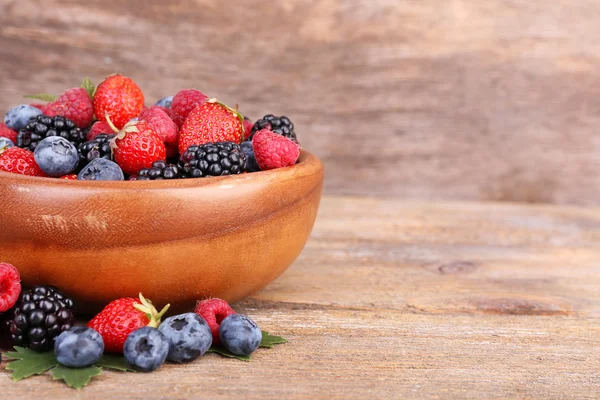 Reife süße verschiedene Beeren in Schüssel, auf altem Holztisch — Stockfoto