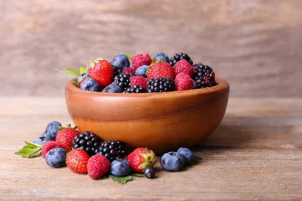 Ripe sweet different berries in bowl, on old wooden table — Stock Photo, Image