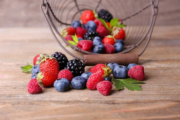 Ripe sweet different berries in metal basket, on old wooden table — Stock Photo, Image