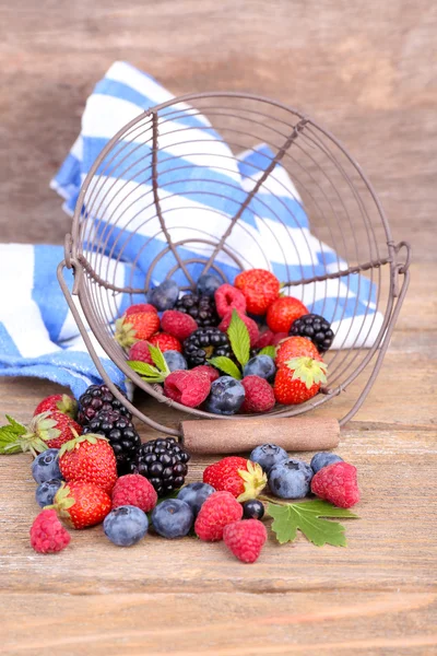 Ripe sweet different berries in metal basket, on old wooden table — Stock Photo, Image