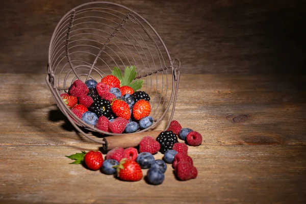Ripe sweet different berries in metal basket, on old wooden table