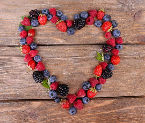 Herz aus reifen süßen verschiedenen Beeren, auf altem Holztisch — Stockfoto