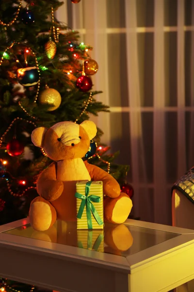 Тедди медведь в интерьере дома на фоне украшенной елки — стоковое фото