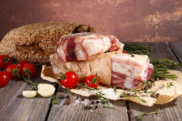 Raw bacon with spices and tomatoes on wooden table — Stock Photo, Image