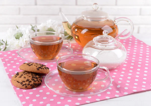 Teapot and cups of tea on table on brick wall background