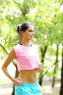 Genç bir kadın parkta koşuyor.