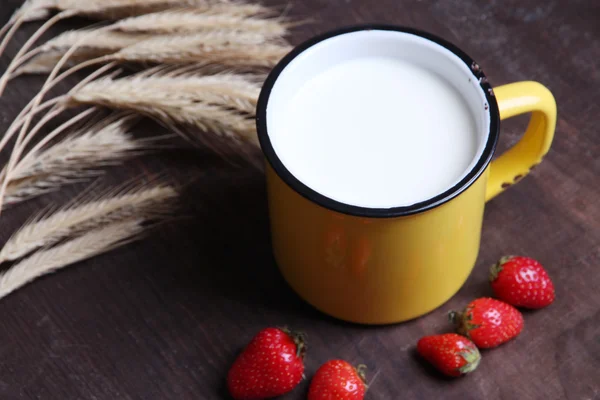 Reife süße Erdbeeren in Holzschale und Becher mit Milch auf farbigem Holzhintergrund — Stockfoto