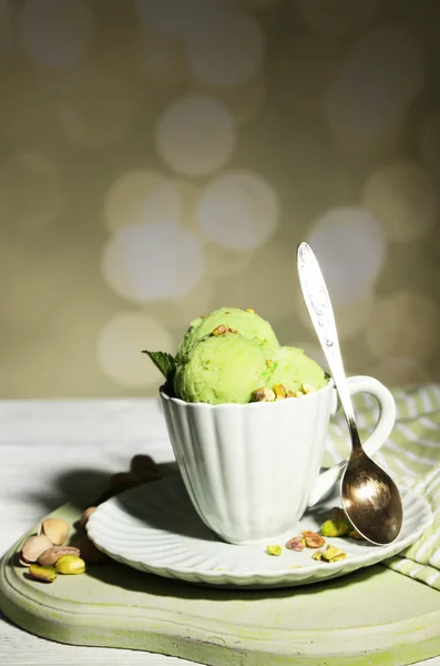Chutnou pistáciovou zmrzlinou v poháru na dřevěný stůl, na světlé pozadí — Stock fotografie