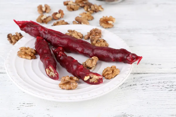 Sabrosos dulces orientales (churchkhela) y nueces frescas en el plato, sobre fondo de madera —  Fotos de Stock