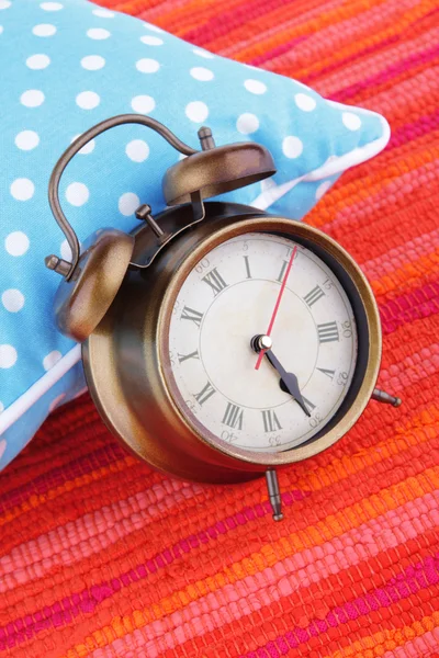 Metal clock on a blue polka dot pillow on red background — Stock Photo, Image